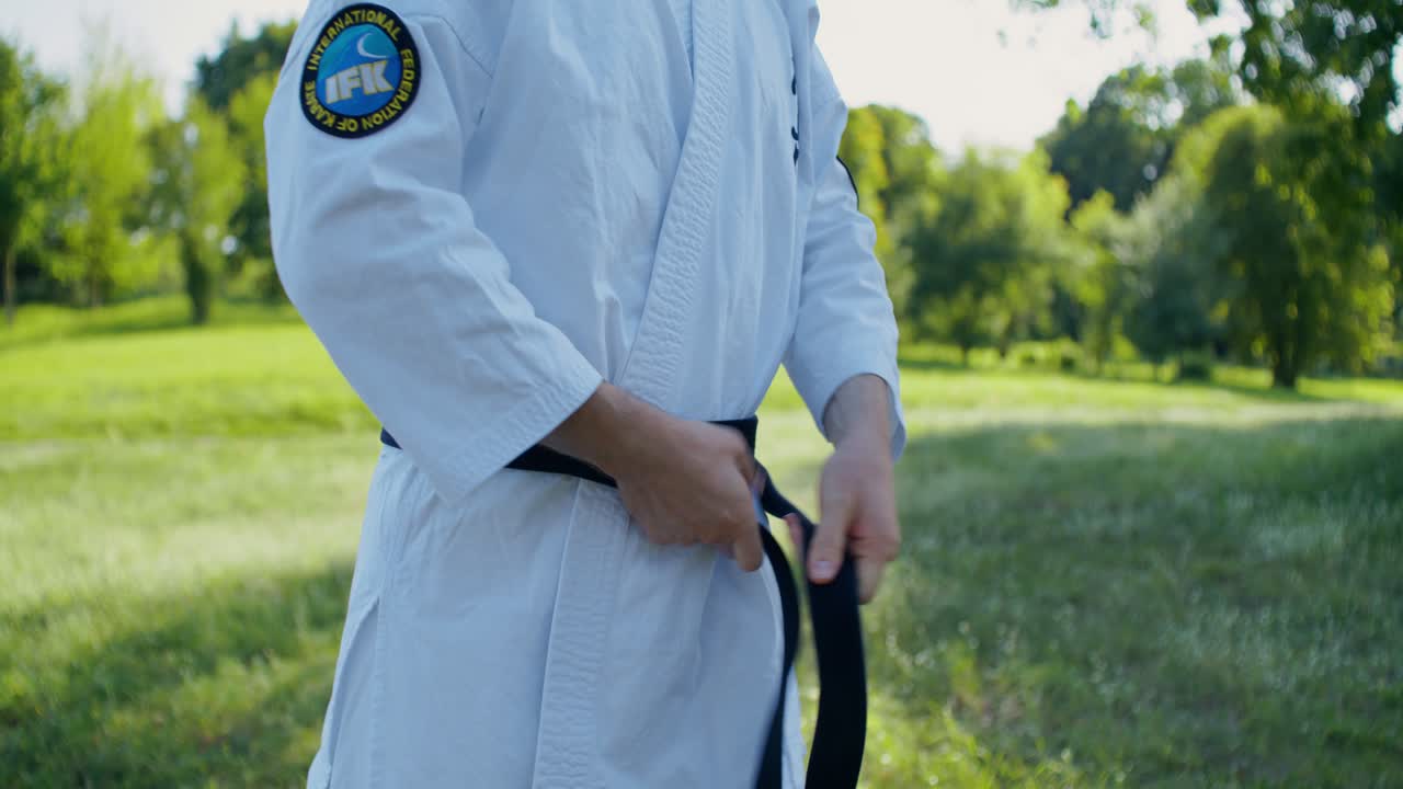 Praticante di karate che allaccia la cintura nera all'aperto