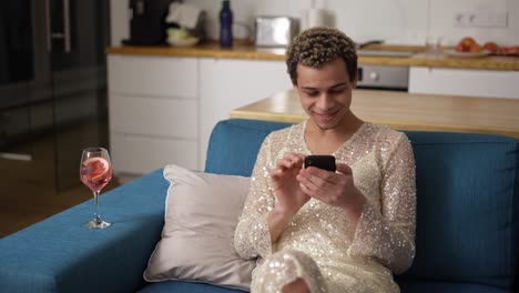 relaxful homosexual guy in fancy dress on a couch using mobile phone