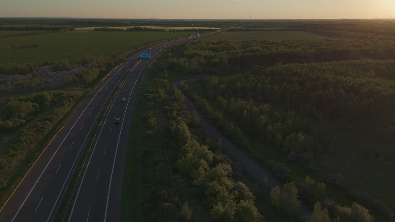 Cinematic sunset drone footage of a highway cutting through fields and forests near Leipzig, Germany. Warm evening light and moving cars create a peaceful yet dynamic travel scene.