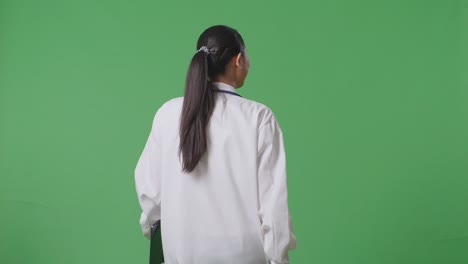 back view of asian female doctor with stethoscope holding a tablet while walking on green screen background in the hospital