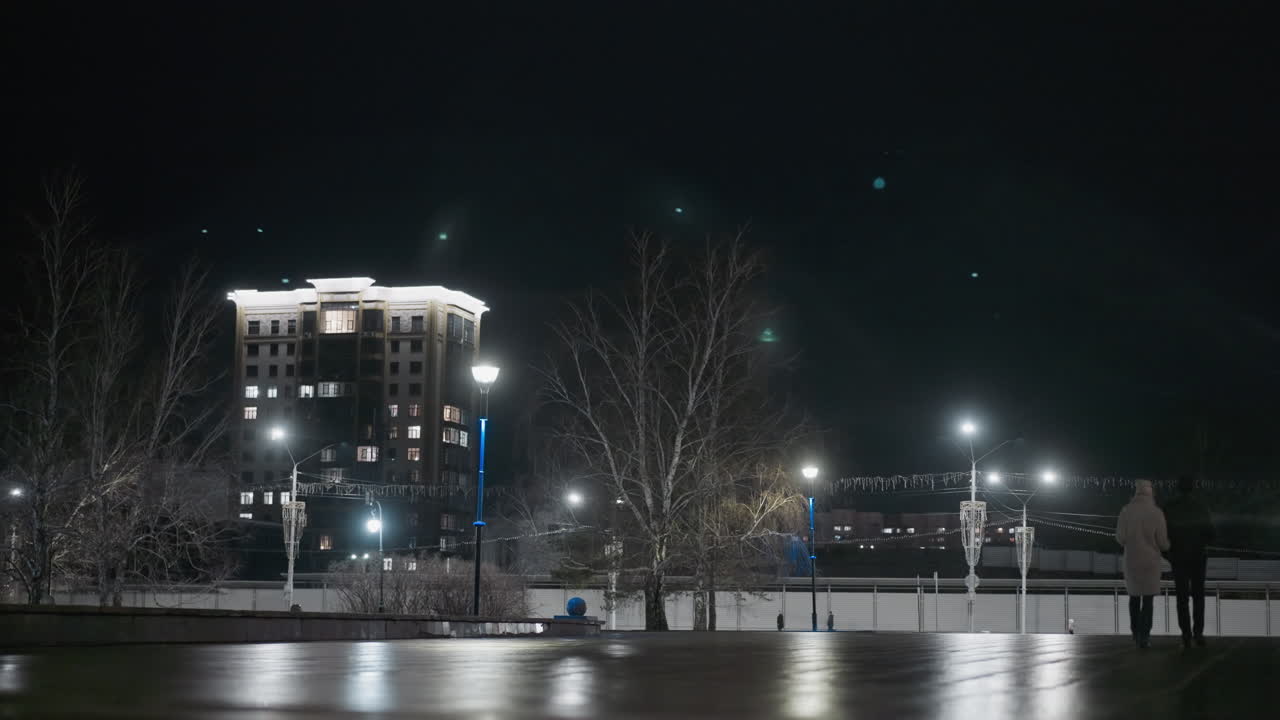 길거리 조명 과 높은 건물 을 배경 으로 하여 조명 된 도시 지역 을 지나가는 사람 들 의 밤 의 모습