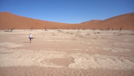 slomo wide of young millenial woman in deadvlei surrounded by dead trees against a blue sky