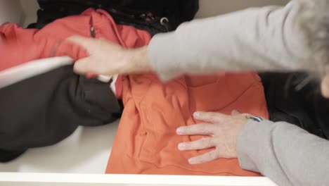 anonymous thief opening a drawer full of hoodies, searching and finding a wad of cash , stealing it and closing the compartment