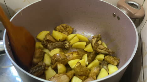 revolviendo chisporroteantes trozos de pollo al curry con papas cortadas en cubitos en una olla con una cuchara de madera