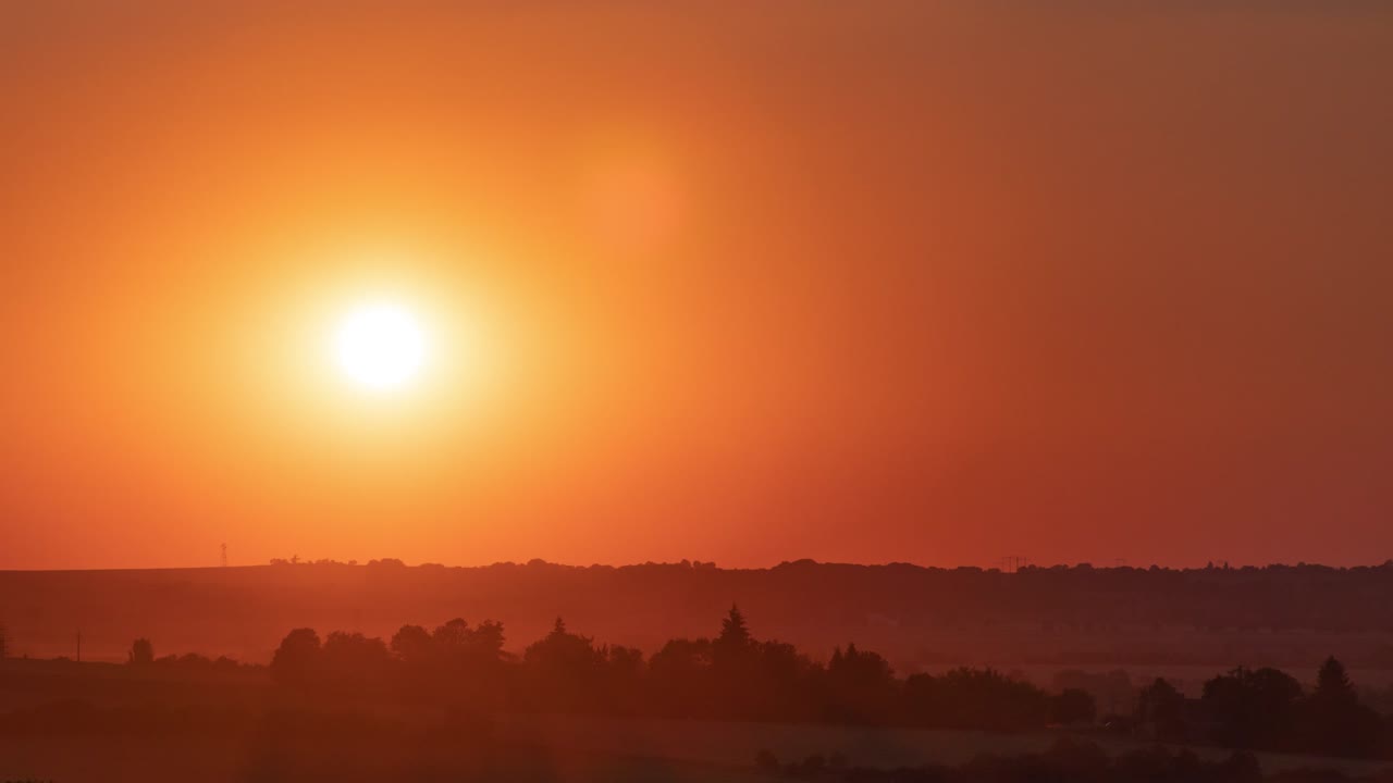 Sunset timelapse with small portion of surroundings including vanishing clouds and lens flares in the beginning and orange rays and wind gusts at the end, framing following the sun
