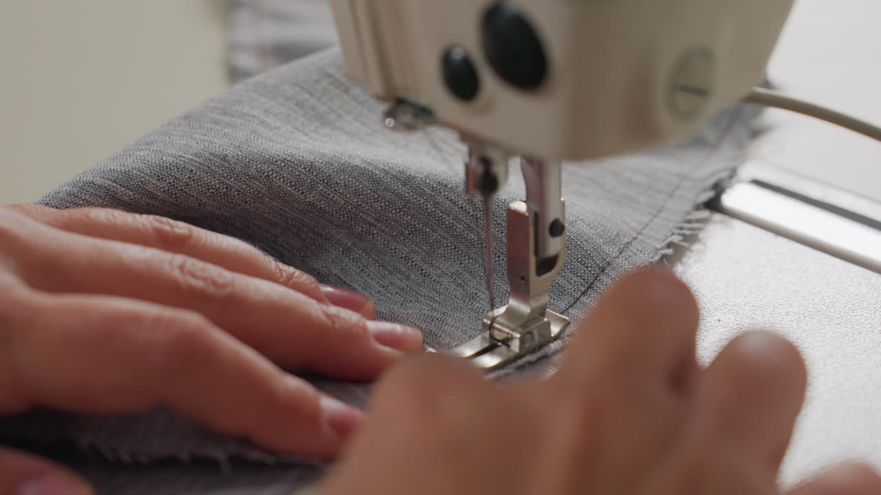 Closeup of female hands guiding wool fabric under sewing machine needle during precise stitching process, showcasing craftsmanship, textile handling, and focus in a well-lit tailoring environment