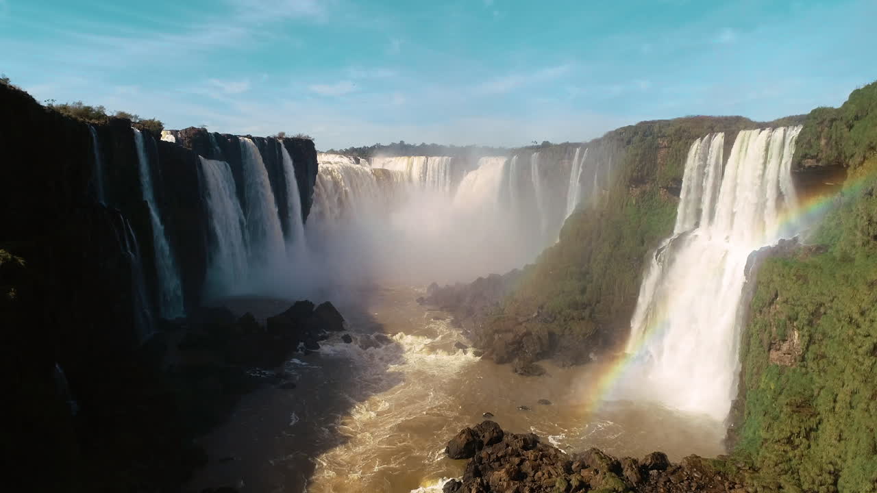 Bird's-eye view gracefully approaches the magnificent Iguazu Falls on a clear blue sky day, capturing the awe-inspiring beauty of this natural wonder