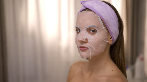young woman wearing a sheet face mask and headband