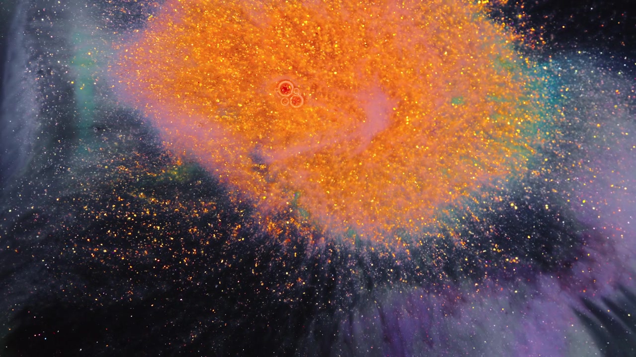 Pigmento de glitter laranja explode na água enquanto rastos de tinta roxa e verde desaparecem num fundo escuro