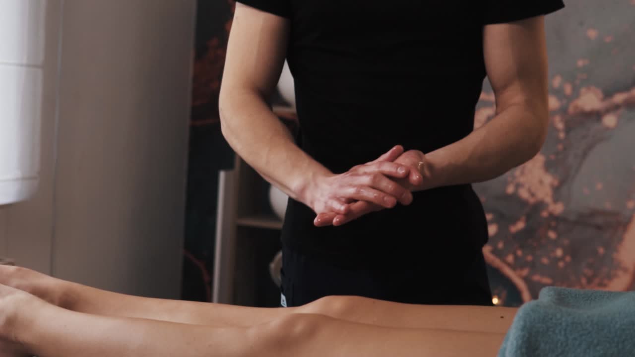 Massøren gnider massageolie ind før behandlingen mod en baggrund af smukke kvindeben.