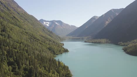 aerial footage of a flight over a huge lake between the mountains with the vast pine forests on both sides in alaska