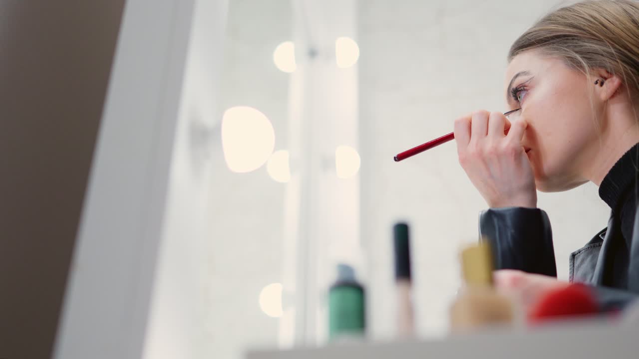 Woman applying makeup with a brush in front of a mirror