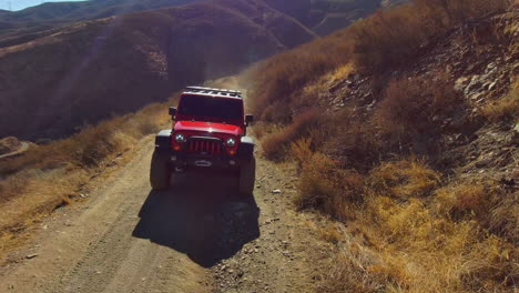 Front-aerial-view-of-red-jeep-offroading-turns-on-and-off-headlights,-desert