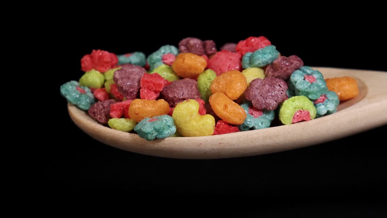 Vibrant cereal pieces tumble from a wooden spoon against a black background, captured in slow motion