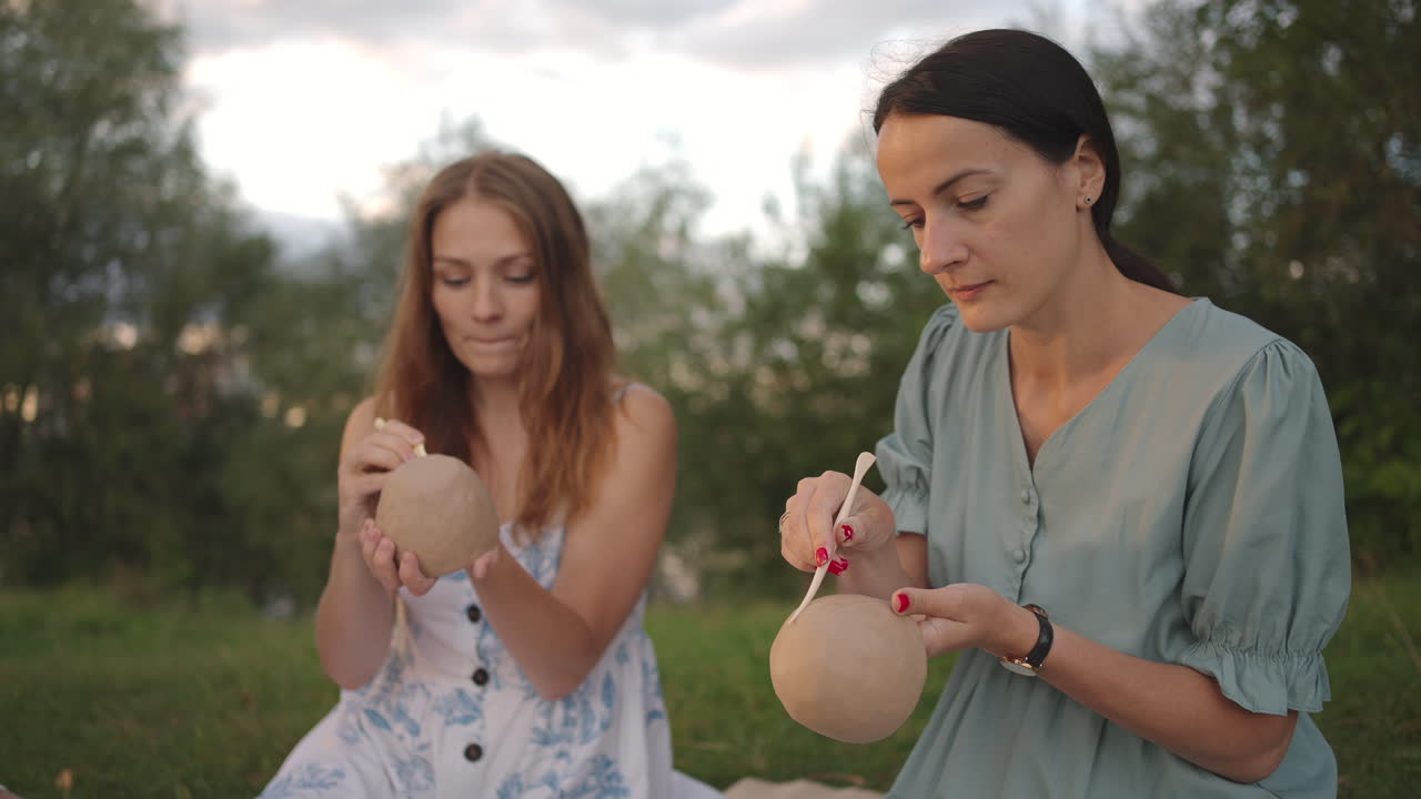 un grupo de mujeres jóvenes se concentran en aplicar patrones a productos de arcilla con la ayuda de herramientas en un prado en la naturaleza en un parque en un espacio abierto. actividad creativa pasatiempo conjunto.