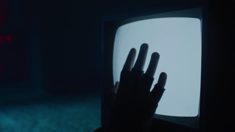 gloved hand touching an old television screen in the dark