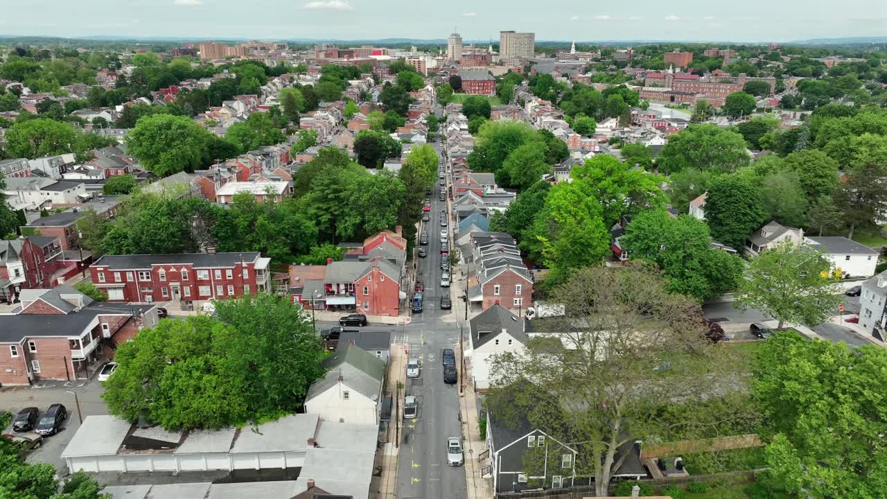 Aerial flyover straight street in small american town with cars on street. Sunny day in May. Historic row of homes and downtown in distance. Forward drone shot. Suburb district of Lancaster.