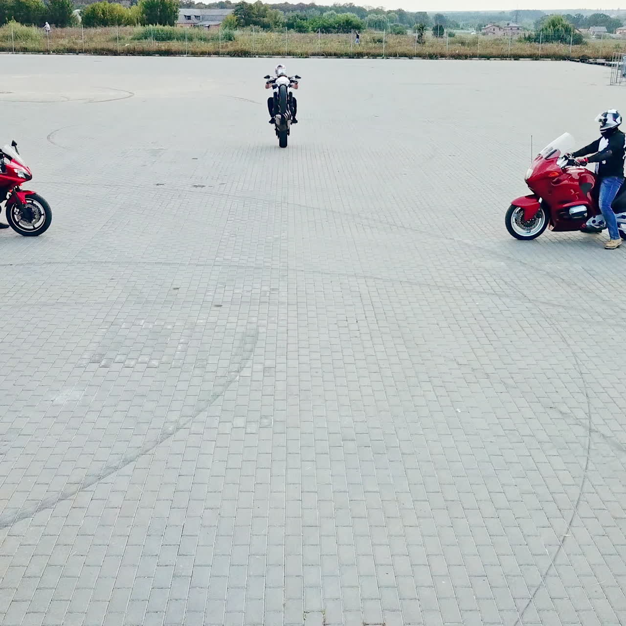Professional motobiker is riding on one wheel on a high speed on the background of two other bikers. Men in special clothes and helmets driving sport motorcycles on a racing track outdoors.