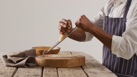 Video-of-mid-section-of-african-american-man-grating-parmesan-cheese-onto-wooden-board-on-table