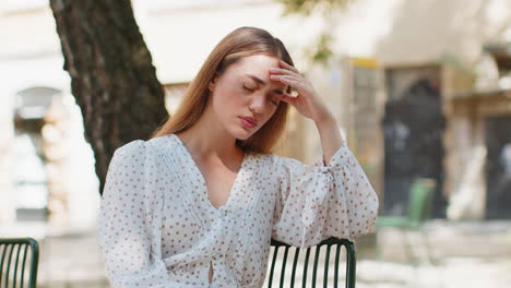 woman rubbing temple to cure headache problem suffering from tension migraine stress on city street