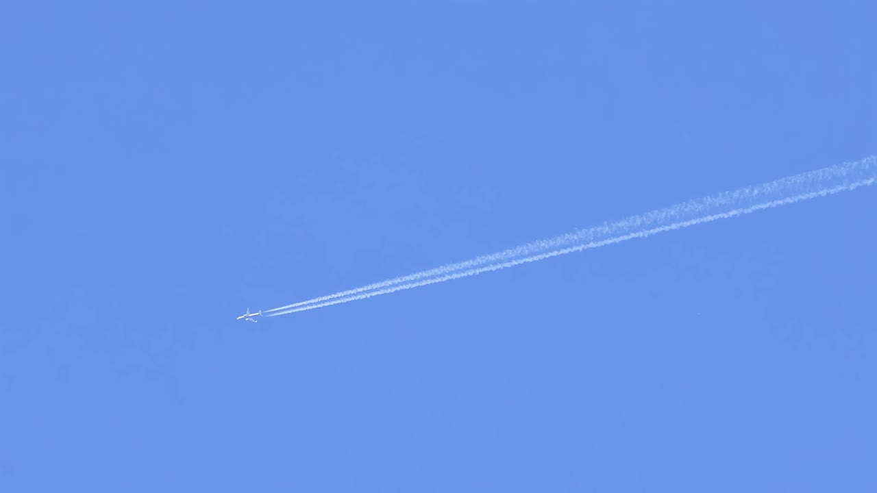 A jet aircraft leaves a distinct contrail against a bright blue sky, showcasing high-altitude flight.