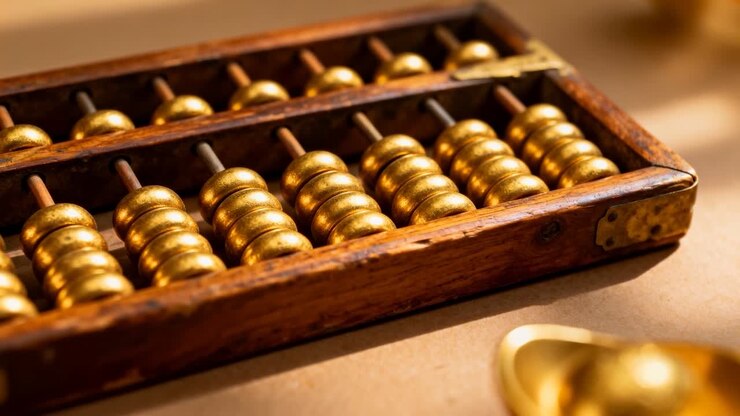 Showing wooden abacus sitting on beige surface, camera shifting focus lighting gold beads and ingot