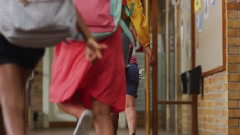 Diverse-group-of-schoolchildren-wearing-backpacks,-running-fast-through-school-corridor