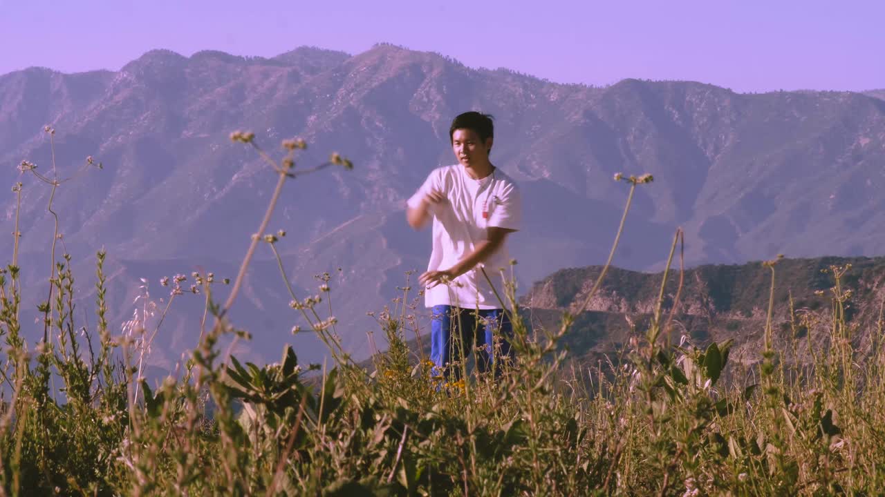 보라색 하늘과 풀이 무성한 전경을 배경으로 산에서 잠그고 홈을 파는 아시아 남성 스트리트 댄서