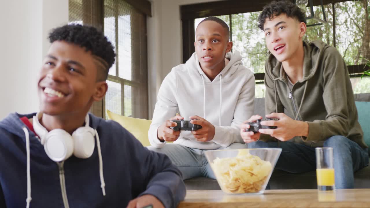 Happy diverse male teenage friends playing video games at home, slow motion