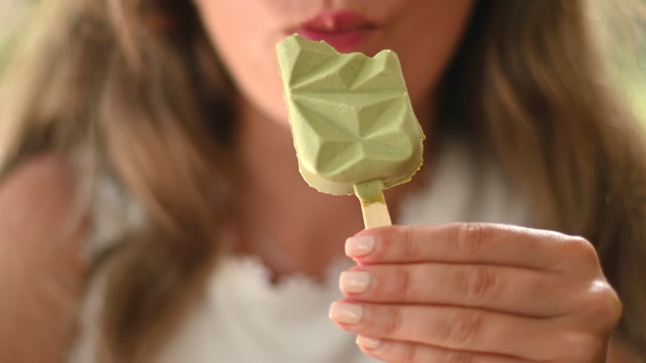 Primo piano di una donna bruna che mangia un gelato verde in un bar, alla luce del giorno