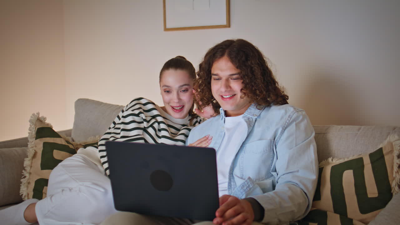 Smiling couple choosing movie to home watching on laptop at couch closeup