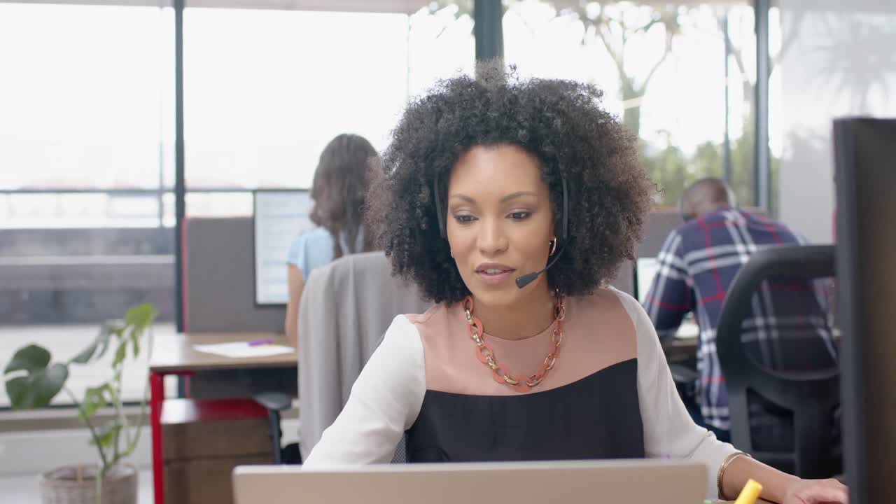 African american woman talking on phone headset and using laptop at office