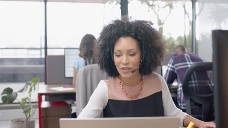 african american woman talking on phone headset and using laptop at office