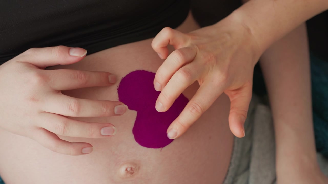 Primo piano di donna incinta che applica taping kinesiologico a forma di cuore.