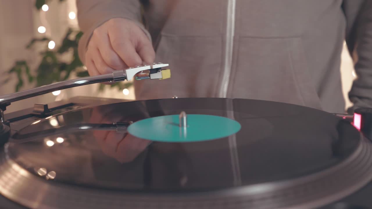 밝은 파티 불빛을 배경으로 dj 회전 레코드 플레이어에 회전 비닐 판의 조각. dj는 음악 플레이어에 접근하고 바늘로 스타일러스를 넣습니다.