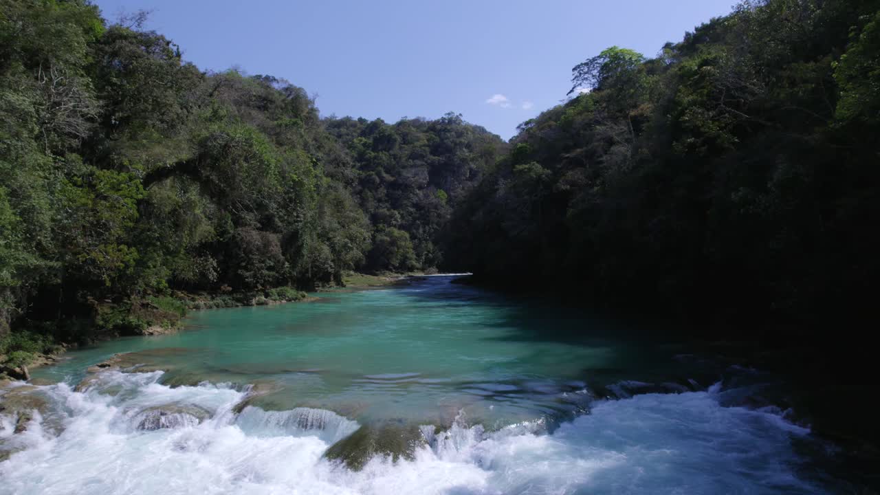 Volo all'indietro vicino all'acqua turchese di un fiume nel mezzo della giungla, attraversando una piccola cascata.