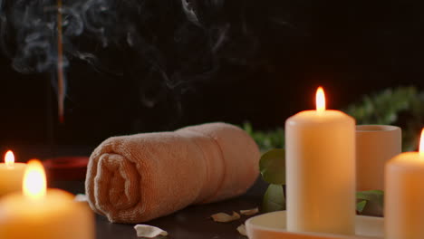 still life of lit candles with green plant incense stick and soft towels against dark background as part of relaxing spa day decor