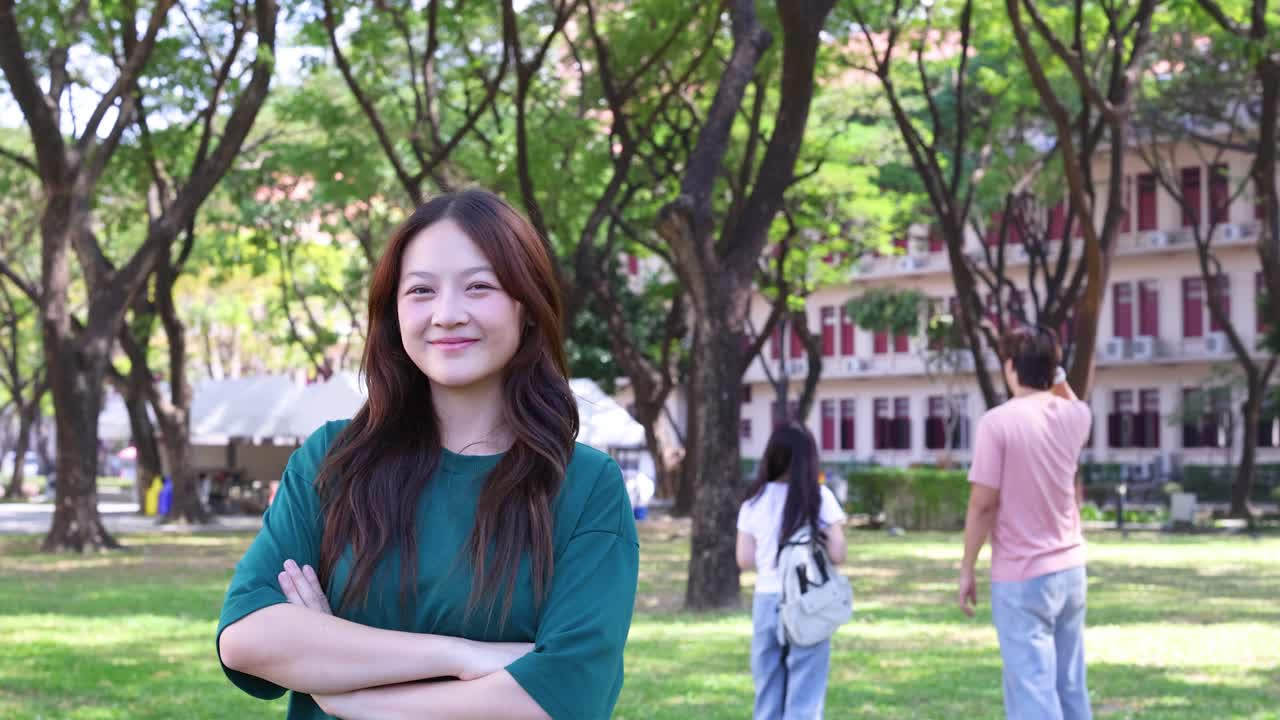 緑のシャツを着た若いアジア人女性が、屋外で微笑みながら腕を組んでいます。