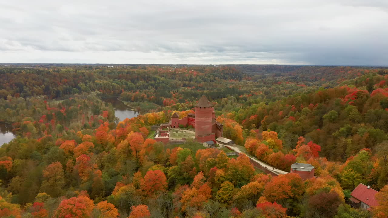 vista aérea del paisaje otoñal del antiguo castillo de turaida, rodeado de bosques de colores amarillo brillante, naranja y árboles verdes, día soleado