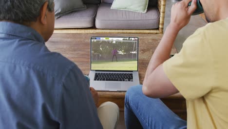 biracial father and son watching laptop with diverse male soccer players playing match on screen