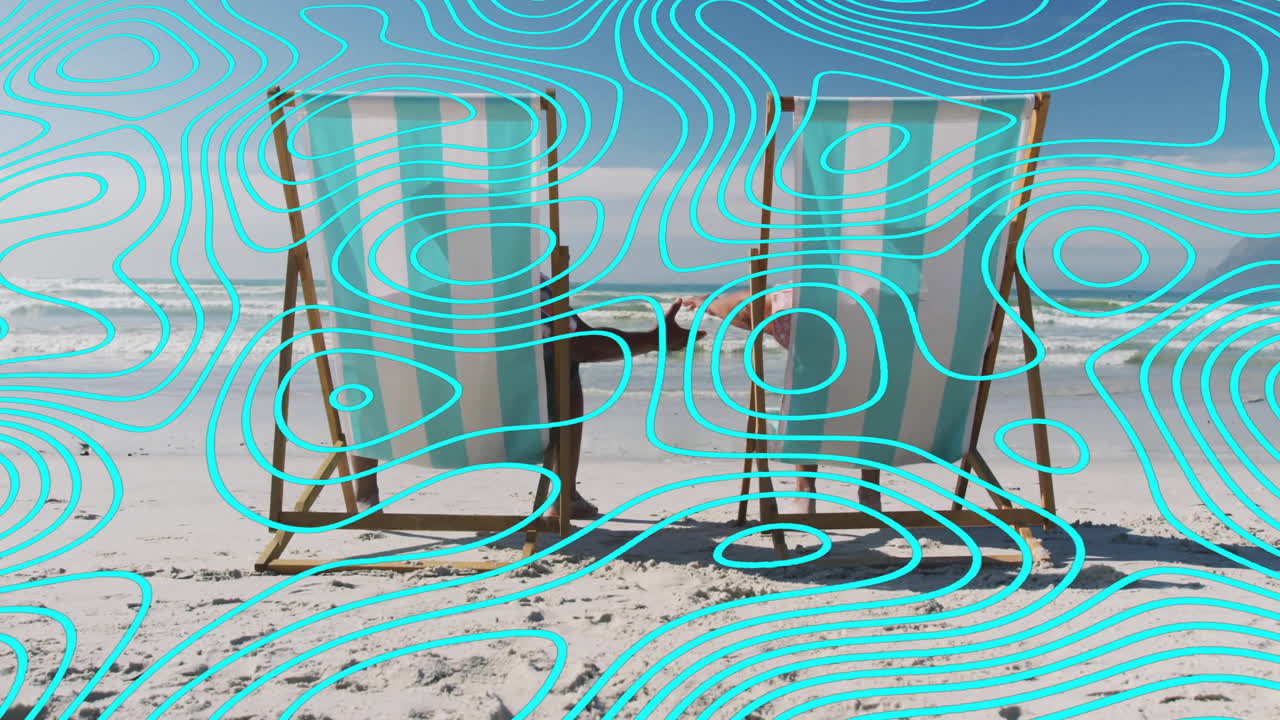 Couple sitting on deck chairs at shoreline, holding hands behind chairs displaying travel icons