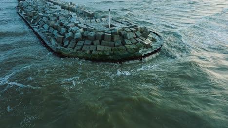 Aerial-establishing-view-of-protective-stone-pier-with-concrete-blocks-and-rocks-at-Baltic-sea-coastline-at-Liepaja,-Latvia,-strengthening-beach-against-coastal-erosion,-drone-shot-moving-back