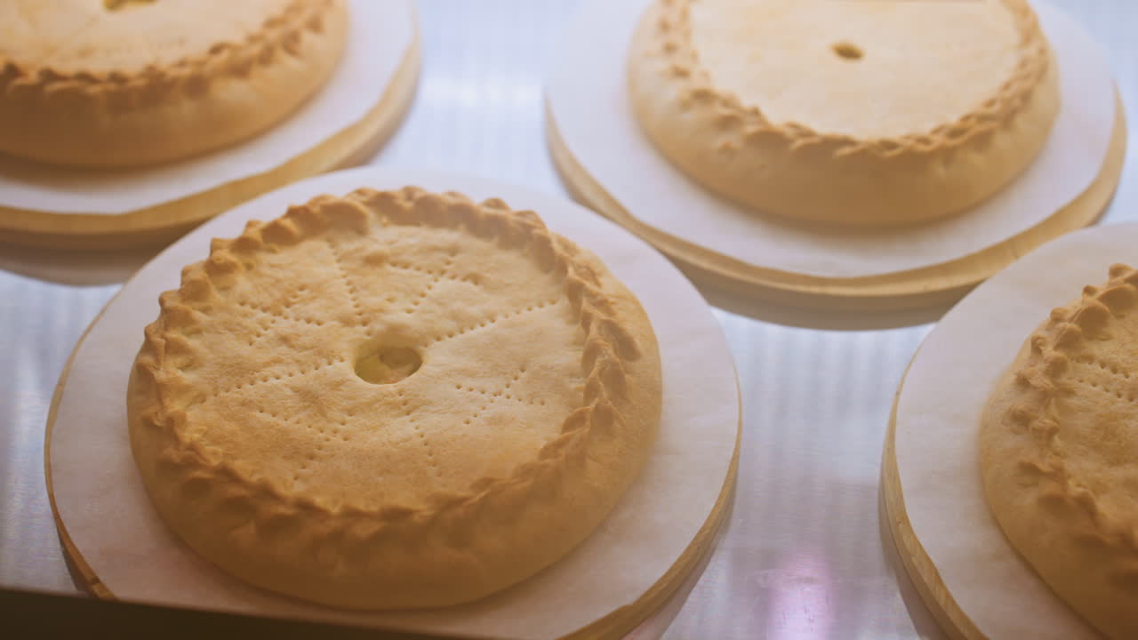Torte pan di Spagna dorate esposte su uno scaffale, cime cotte uniformemente e consistenza morbida sotto le luci calde della pasticceria, semplici dessert disposti su vassoi, una lenta panoramica rivela l'atmosfera accogliente di una pasticceria mattutina.