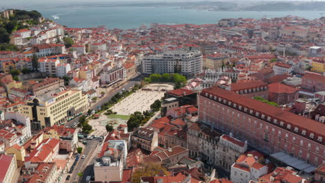 órbita-Aérea-Del-Centro-De-La-Ciudad-De-Lisboa-Con-Casas-Coloridas-Tradicionales-Alrededor-De-La-Plaza-Martim-Moniz,-El-Castillo-De-Lisboa-En-La-Colina-Y-El-Mar-Al-Fondo