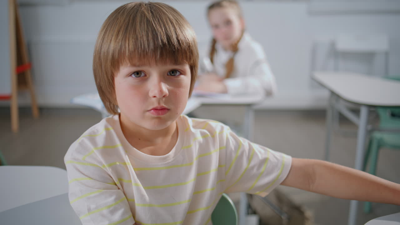 Scolaretto che guarda la fotocamera durante una lezione in classe. Ragazzo che alza la mano
