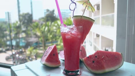 juicy watermelon pieces lie on white table near tall glass