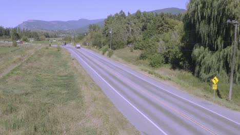 Retención-Aérea-Sobre-La-Leva-De-Seguimiento-De-Camiones-Rojos-Que-Transportan-Gas-Que-Transportan-Un-Petrolero-Plateado-En-Una-Autopista-Suburbana-Autopista-Tarde-De-Verano-Valle-Tierras-Montañosas-Campo-1-2