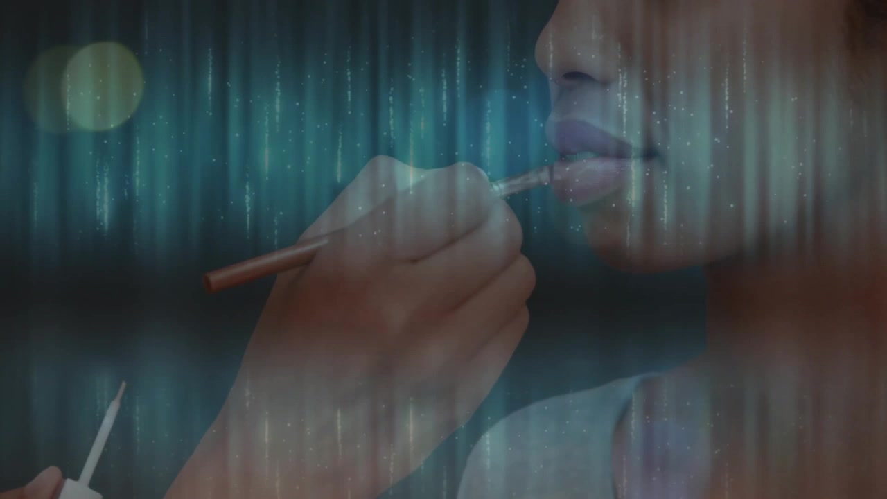 Makeup artist priming lips brushing rosy tint on model lips over turquoise lights for beauty look
