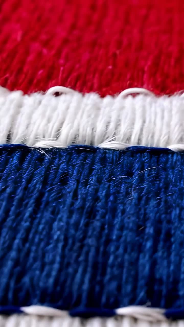 Video verticale: obiettivo macro che rivela un pezzo di tessuto su una scrivania con cuciture rosse, bianche e blu
