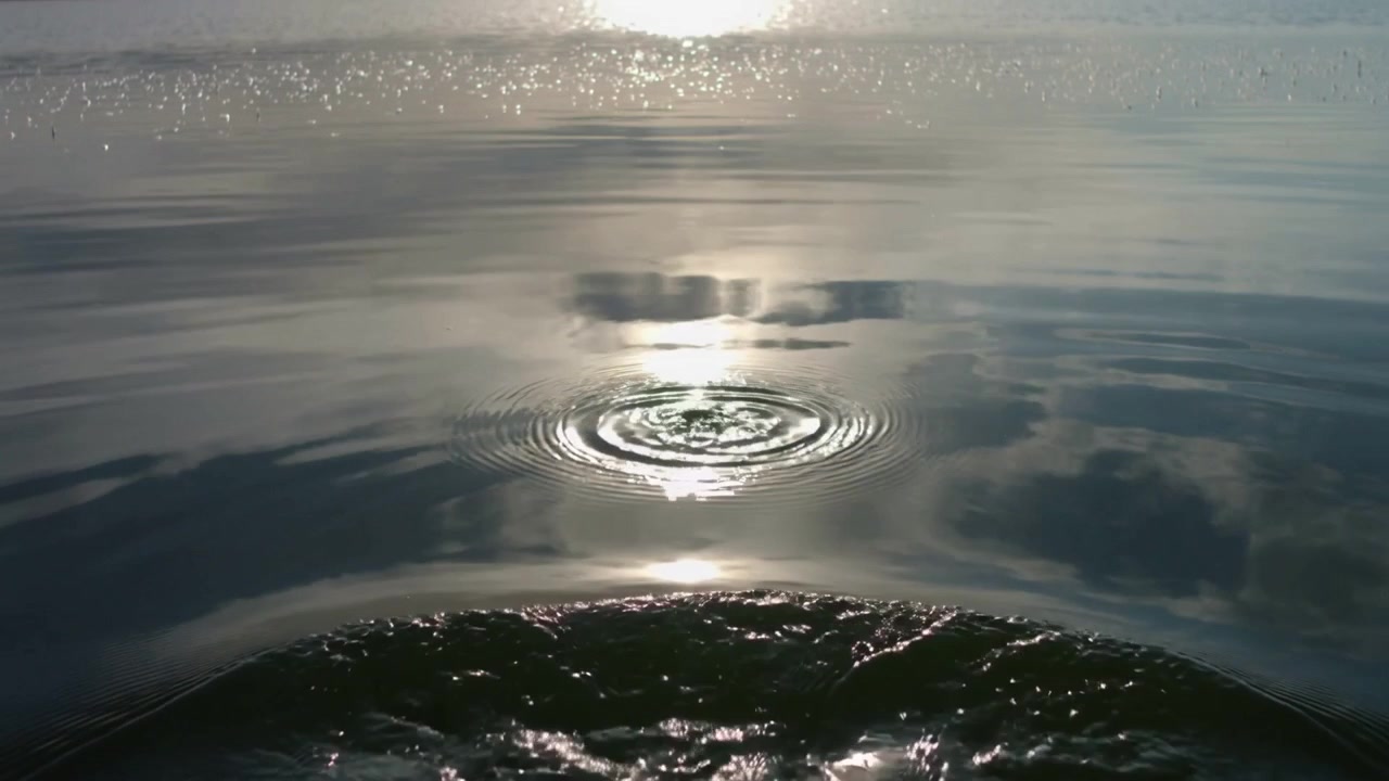 Una depressione che crea increspature circolari sull'acqua vicino all'orizzonte, con il riflesso del sole e una prua bagnata.